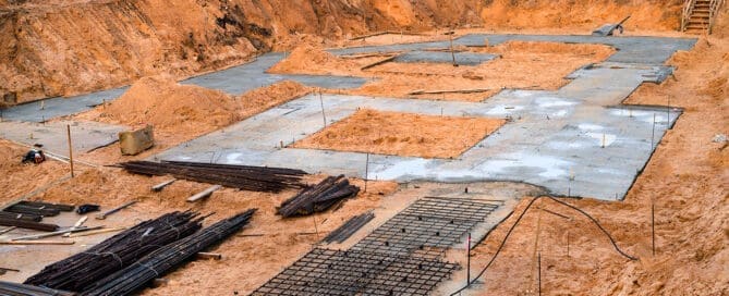 Excavated construction site with concrete footings, rebar, and sand foundation preparation.
