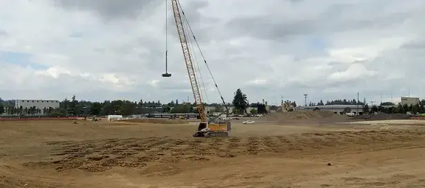 Liebherr crane performing dynamic compaction at a construction site in Oregon, with impact zones visible on the compacted soil surface.