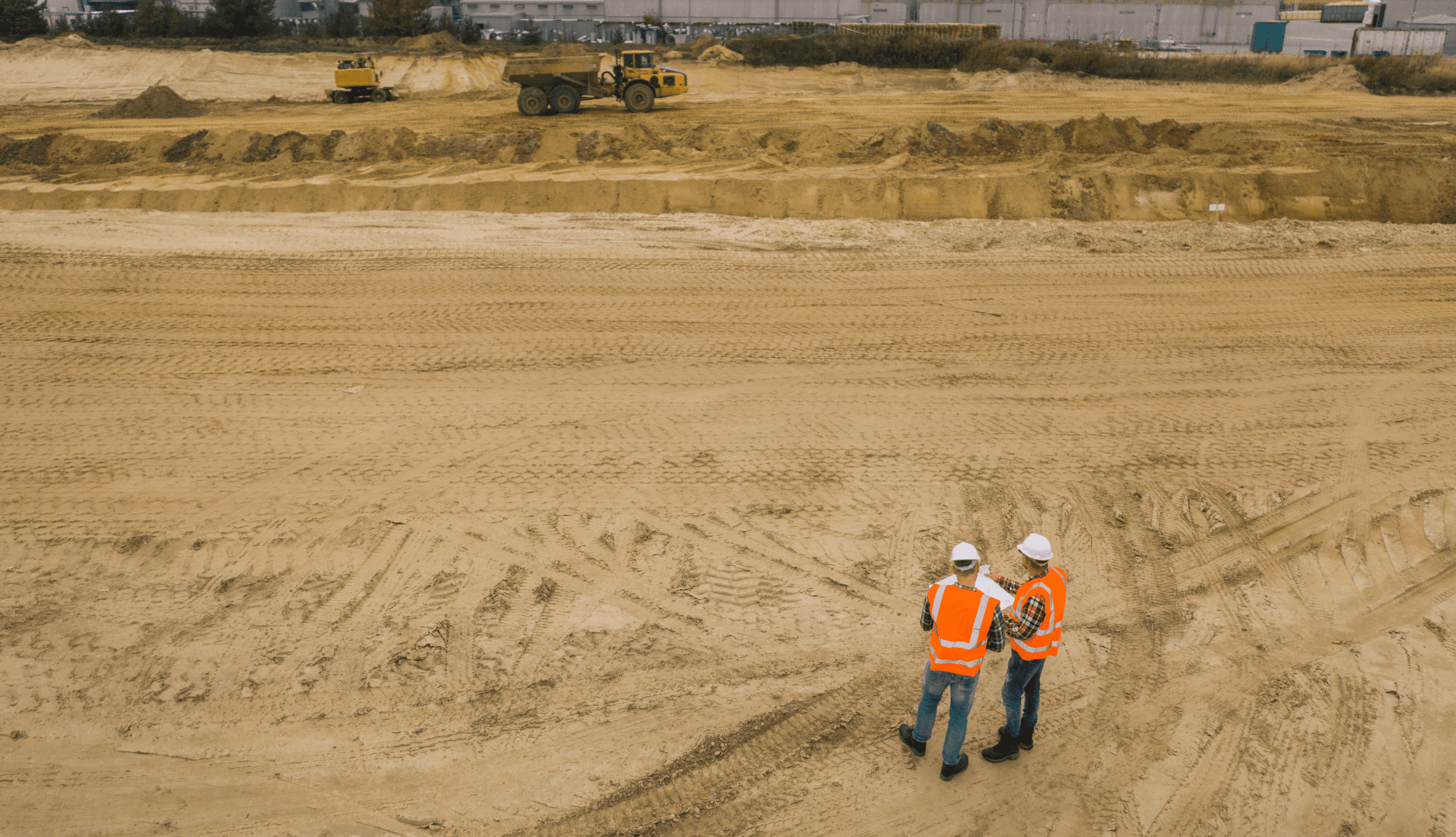 Two road construction workers in orange vests and protective helmets in the middle on the field