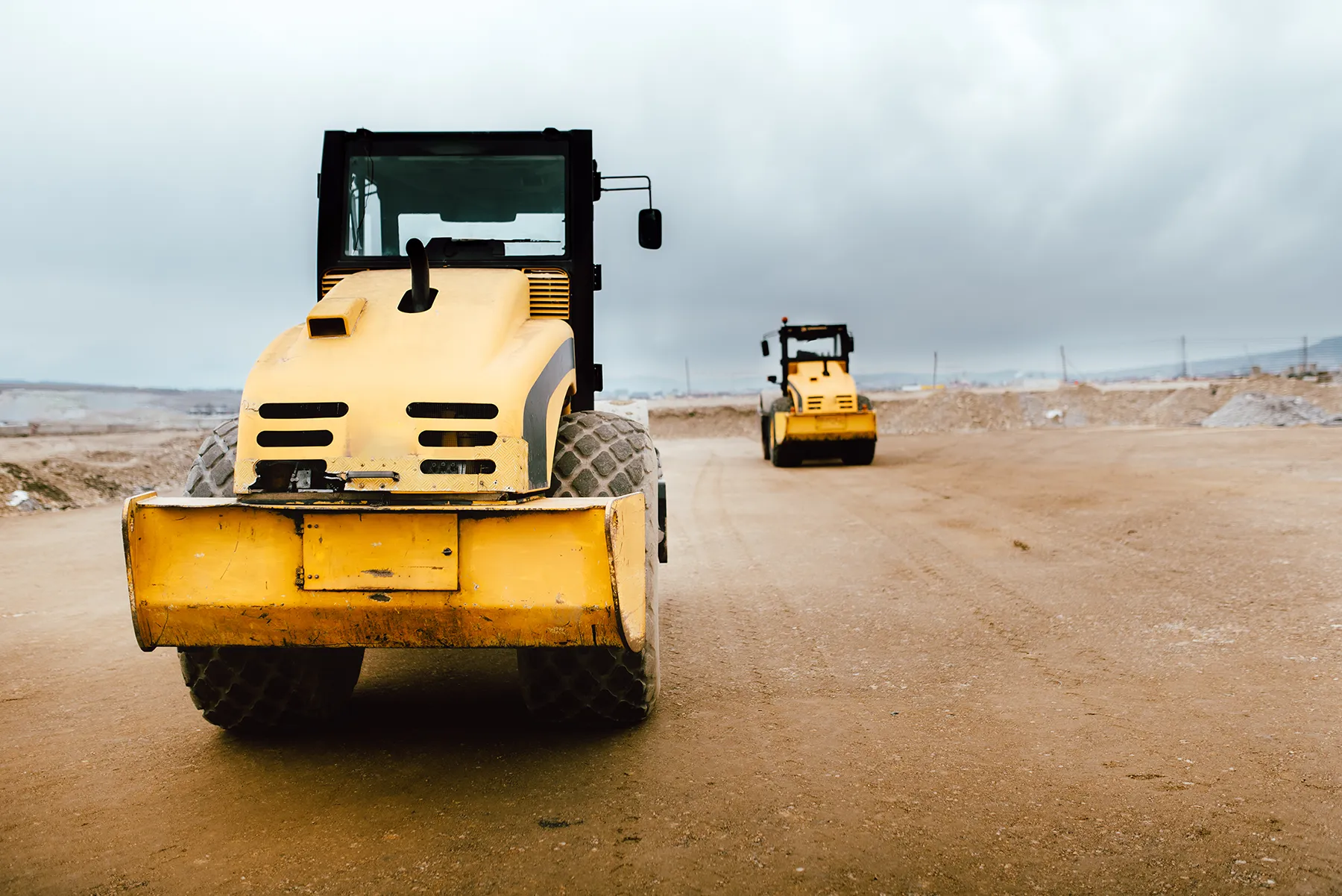 Two Vibratory Soil Compactors on construction site. Industrial roadworks at highway with heavy-duty machinery Two Vibratory Soil Compactors on construction site. Industrial roadworks at highway with heavy-duty machinery