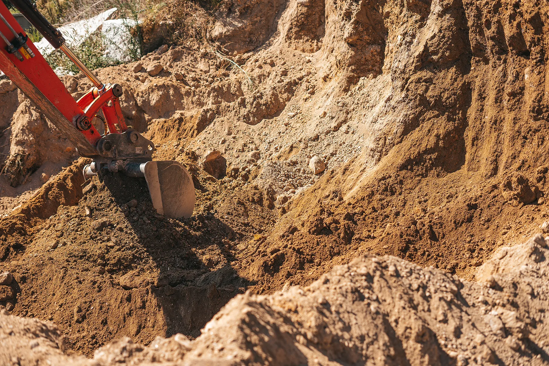 Excavator shovel digging into soil at a construction site.