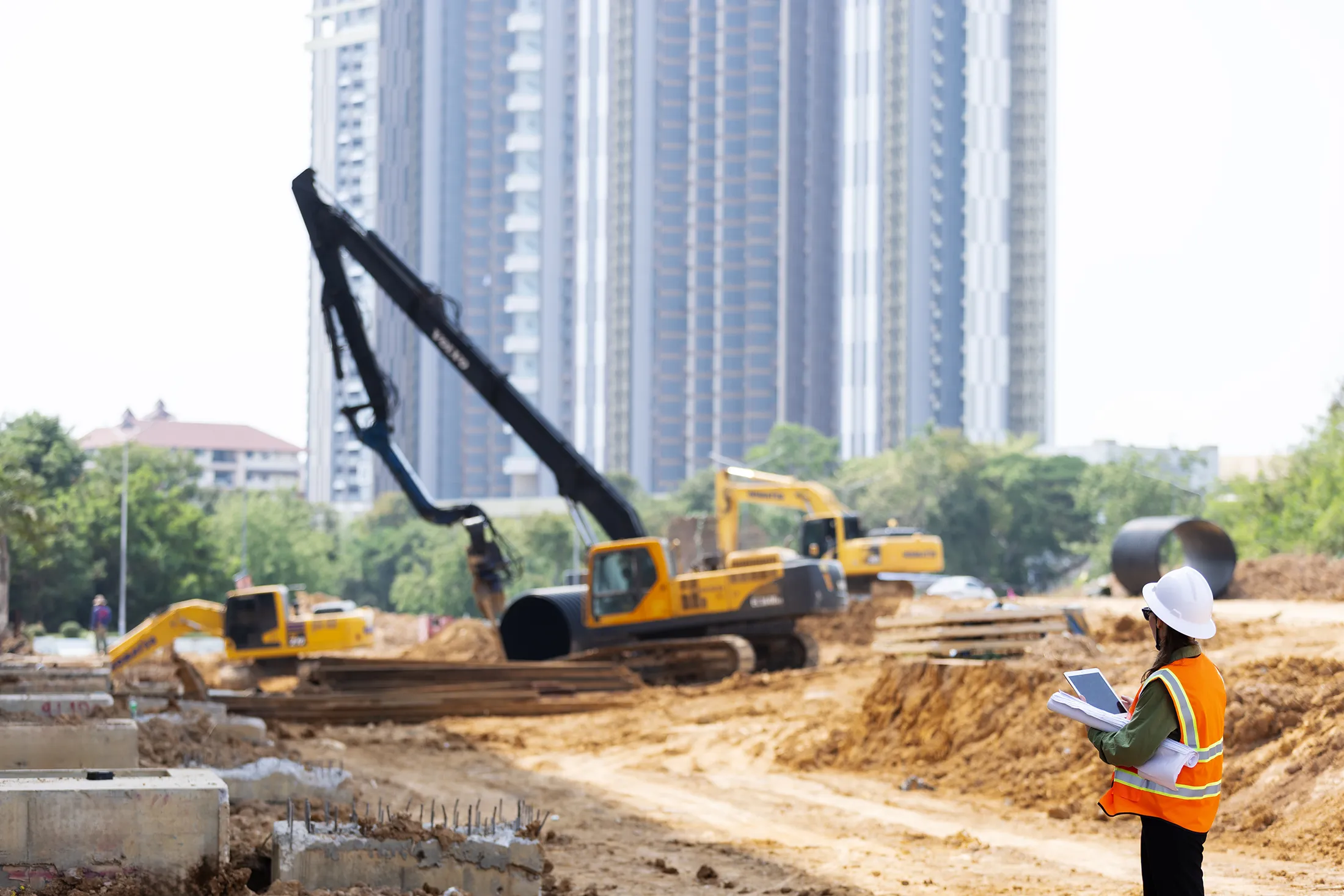Construction site with heavy excavation equipment and cranes performing ground improvement work, while an engineer reviews plans in the foreground.